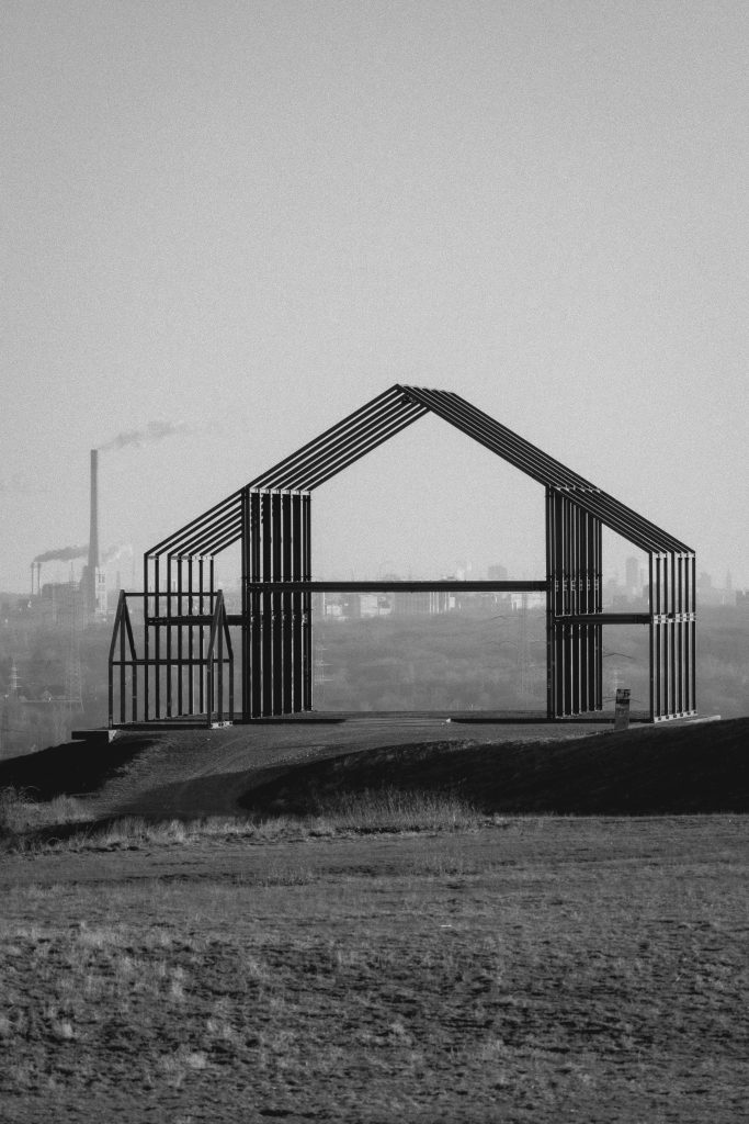 Monochromatic view of a metal frame structure on a hillside with industrial landscape in the background.
